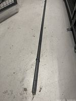 Full length view of metal barbell on concrete floor, showing black textured surface and wear.