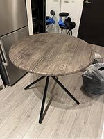 Full view of the round table showing the wood grain veneer top and black metal tripod legs