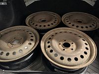 Four steel wheels with surface rust placed in a vehicle trunk, showing the top surfaces and general condition.