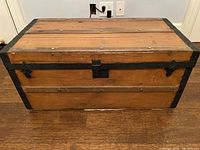 Front view of the antique wooden chest showing wooden panels and iron bands around the edges. Central iron lock without key is visible along with two side latches.