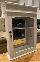 Front side view of a white curio cabinet with glass door, mirror backing, metal hardware, and visible adjustable shelf inside.