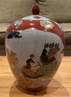 Front view of oval-shaped ceramic vase featuring colorful hand-painted peacocks, flowers, and foliage with gold highlights and crackle glaze.