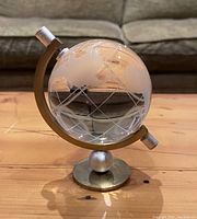 Front view of etched glass globe on curved metal stand with circular base, showing details of etched continents and grid lines.