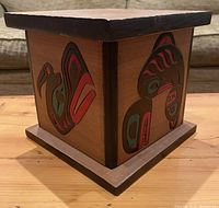 Side view of large red cedar bentwood box showing Thunderbird and Killer Whale carved and painted designs in black, red, and greenish-blue.