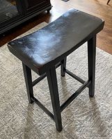 Black oak bar stool shown from top angled view highlighting curved seat and wear on edges.
