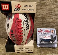 Mini Wilson CFL football in box, visible logos for 95th Grey Cup Toronto 2007, Wilson label and CFL branding. Next to it is the packaged Tim Hortons Zamboni toy with Sidney Crosby graphics.