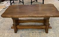 Front view of rustic solid wood coffee table showing carved edges, legs, and support bars. Visible scratches and wear on tabletop.