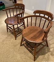 Two matching vintage oak captain's chairs with spindle backs and armrests on carpeted floor.