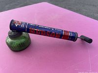 Full view of the antique Hudson pest sprayer showing the green ribbed glass jar and the metal pump tube with branding.