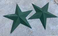 Two green painted metal stars on concrete floor with minor paint wear and weathering.