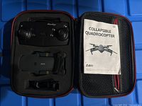 Open carrying case showing black foldable drone, controller, and instruction manual inside foam compartments.
