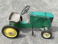Side view of green and yellow steel body pedal tractor showing plastic seat, steering wheel, and wheels