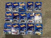 Top-down photo of all 15 Hot Wheels cars in original blue carded packaging, arranged on carpeted floor.