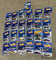 Photo showing 25 carded Hot Wheels cars, mostly hot rods and classics, arranged in rows on the floor.
