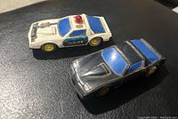 Photo of white police and black firebird slot cars on black surface showing side and top views