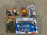 Overview of the lot showing Matchbox cars, yellow fighter jet, helicopters, plastic soldiers, and boxed fighter jets set.