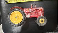 Side view of vintage red diecast Massey Ferguson toy tractor showing large rear yellow wheel and smaller front wheel.