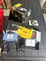 Photo of Nikon COOLPIX E990S camera and accessories laid out on table including original box, battery, camera case, USB cable, software CD, manuals, and strap.