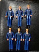 Six vintage Tonka garage action figures arranged in two rows, with blue uniforms and blonde hair, on a black textured surface.