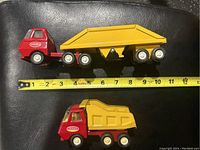 Two vintage Tonka trucks on black surface with measuring tape showing length of about 11.5 inches for the semi-truck