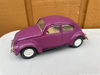 Side angle showing purple metal diecast Volkswagen Beetle model car with white wheels and metal bumpers on white surface.
