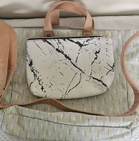 Photo of tan tote bag with leather handles and a glimpse of the white and black purse next to it.