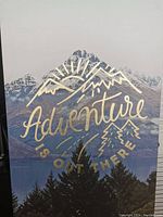 Full frontal view of the canvas art showing the mountain landscape with the gold foil text 'Adventure is Out There' and trees in the foreground.