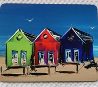 Front view of the placemat showing colorful stylized green, red, and blue beach houses on a sandy shore under a bright blue sky with seagulls