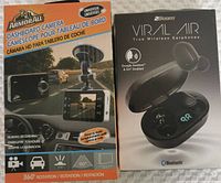 Photo of the front of the box for Armor All dashboard camera and 2Boom Virus Air true wireless earphones side by side on a fabric surface.