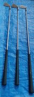 Three Wilson golf irons with black grips laid flat on blue tarp, clearly showing condition and style.