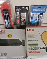 Photo showing all items in lot including QFX DVD player, QFX antenna, two universal remotes, and Eclipse Pro microphone in original packaging.