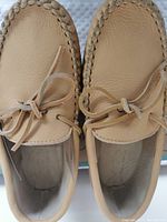Overhead view of the moccasins showing light tan leather tops with lace bows and stitched detailing.