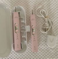 Philips Sonicare electric toothbrush and extra battery, charging stand, power cord, and carrying case displayed on a white textured surface.