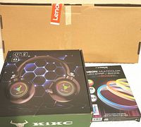Closed boxes of KIKC gaming headphones and neon multicolor LED strip kit, on top of Lenovo keyboard box