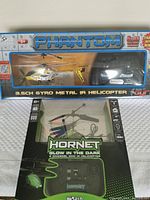 Photo of Phantom and Hornet RC helicopters in original packaging showing the front of the boxes with branding, yellow helicopters visible along with their respective remotes.