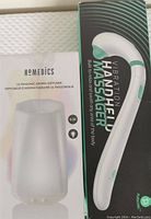 Photo showing original boxed Homedics ultrasonic aroma diffuser with frosted dome shape and the box for the vibration handheld massager side-by-side.