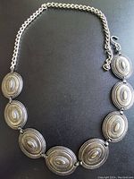 Image of a silver-tone chain belt with seven oval medallions arranged in a row, connected by chain links and a hook closure at the end.