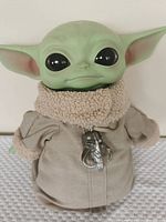 Front view of Baby Yoda plush toy showing facial details, coat collar and pendant accessory.