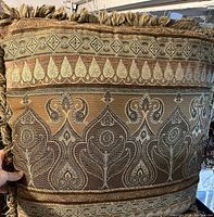 Close-up image showing detailed woven floral and geometric patterns on one of the identical accent pillows, highlighting the textured fabric and fringed tassel trim.