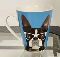 White ceramic mug with a Boston Terrier graphic wearing white glasses on a blue background.