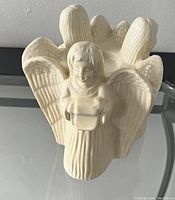 Front view of the white ceramic angel-shaped tealight candle holder with visible detailed wings and angel figure holding a book.