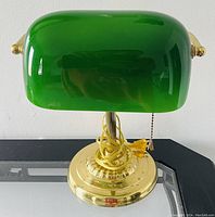Front view of a banker’s lamp with a green glass shade and brass base featuring a pull chain switch.