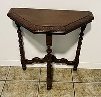 Front view of the vintage demilune accent table showing ornate carved edge, turned legs, and stretcher base detail.