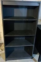 Front view of the black bookshelf showing four shelves and the overall condition.