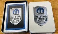 Photo of two silver rectangular tins side by side featuring Mopar 75th Anniversary logo, housing new playing cards.