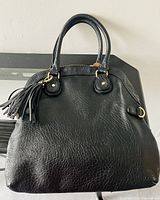 Front view of textured black leather purse with two handles and hanging tassel detail