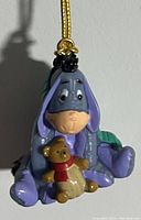 Close-up of vintage Eeyore Christmas tree ornament showing Eeyore holding a teddy bear with a red scarf.