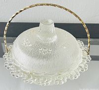 Clear glass candy dish with a hobnail bubble edge and textured lid topped with a knob, with a gold-tone metal carry handle.