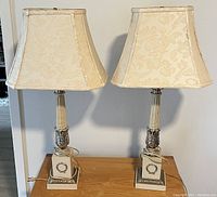 Pair of matching 32 inch table lamps with ornate bases and cream floral fabric shades on wood surface.