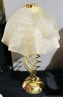 Brass spiral tealight lamp with cream marbled glass shade on black surface